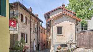 A narrow cobblestone street with historic buildings, a flag, and a stone well. - Holiday Home 'Unit C' by the Lake, Wi-Fi and Air Conditioning (Laveno-Mombello)