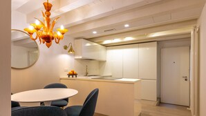 A modern kitchen with white cabinets, a central island, and a dining area with a round table and chairs. - Peaceful Cannaregio Top-Floor Apartment Steps from Ca’ D’Oro (Venice)