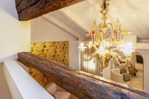 Ein Zimmer mit einer Kristallleuchter, einem Holzbalken, floralem Wandpapier und einem Sofa.