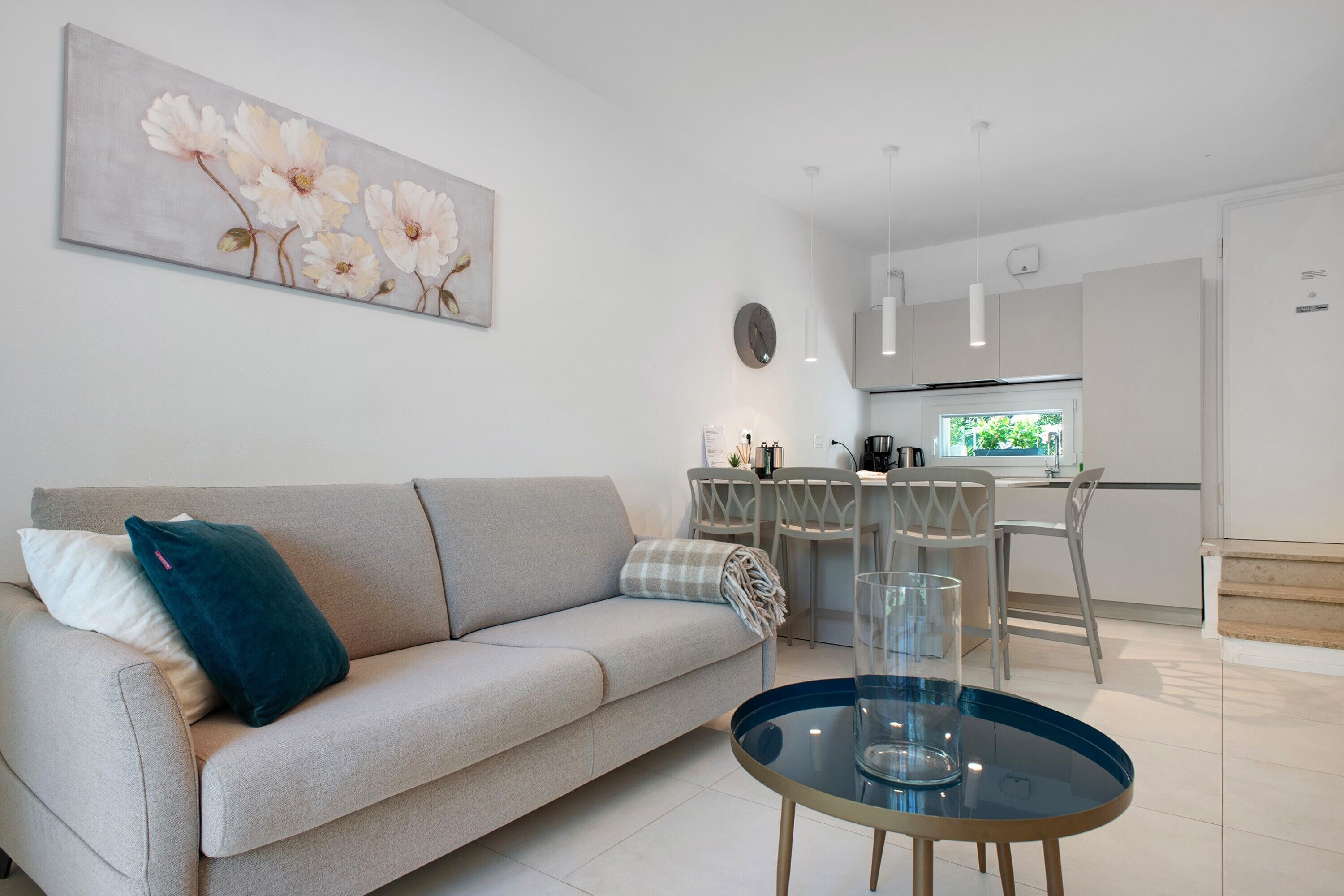 A living room with a sofa, a glass coffee table, and a painting on the wall.