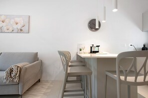 A modern living room with a sofa, a dining area with bar stools, a wall clock, and a minimalist decor.