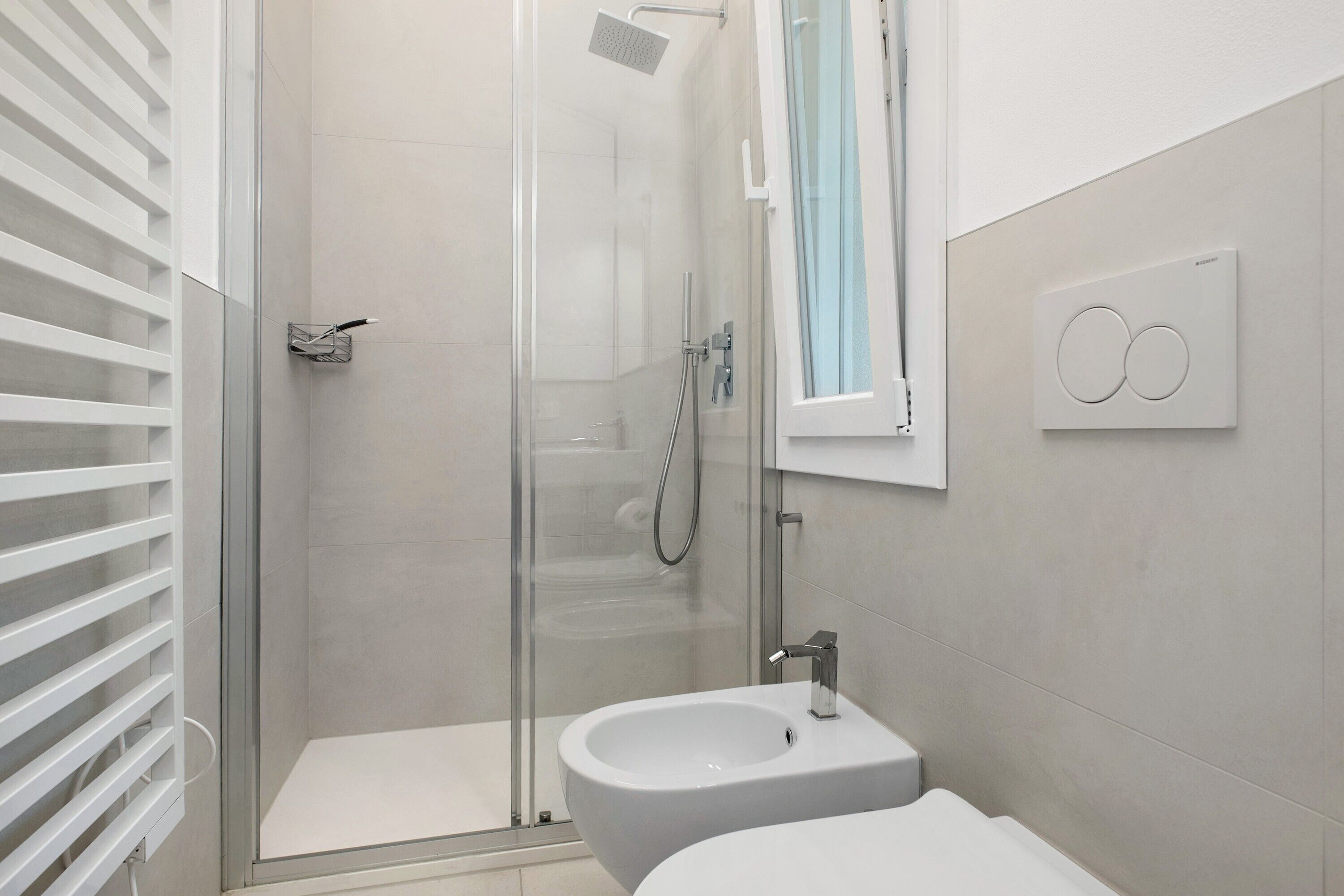 Ein modernes Badezimmer mit einer gläsernen Duschkabine, einem Standwaschbecken und einer Wandleuchte.