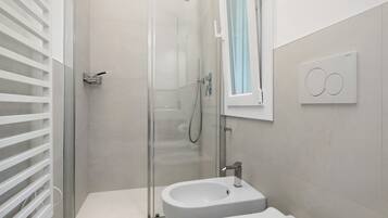 Ein modernes Badezimmer mit einer gläsernen Duschkabine, einem Standwaschbecken und einer Wandleuchte.