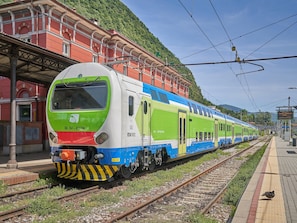A train at a station with a platform, tracks, and a mountainous backdrop. - Holiday Home 'Unit D' by the Lake with Large Garden, Wi-Fi and Air Conditioning (Laveno-Mombello)