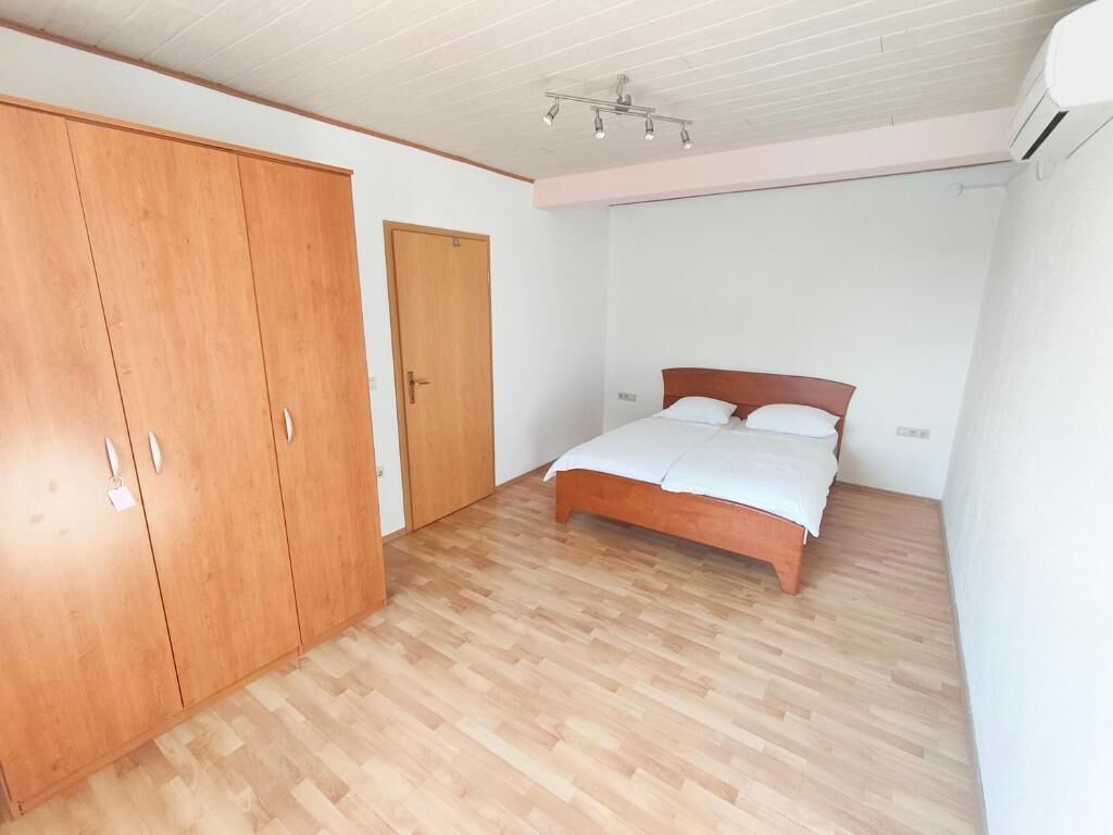 Un dormitorio con un armario de madera, una cama con ropa de cama blanca y suelo de madera.