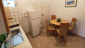 Eine kleine Küche mit Spüle, Kühlschrank, Esstisch mit Stühlen und einem kleinen Fenster.