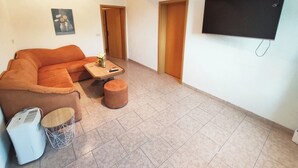 Ein Wohnzimmer mit einer Couch, einem Hocker, einem kleinen Tisch und einem an der Wand befestigten Fernseher.