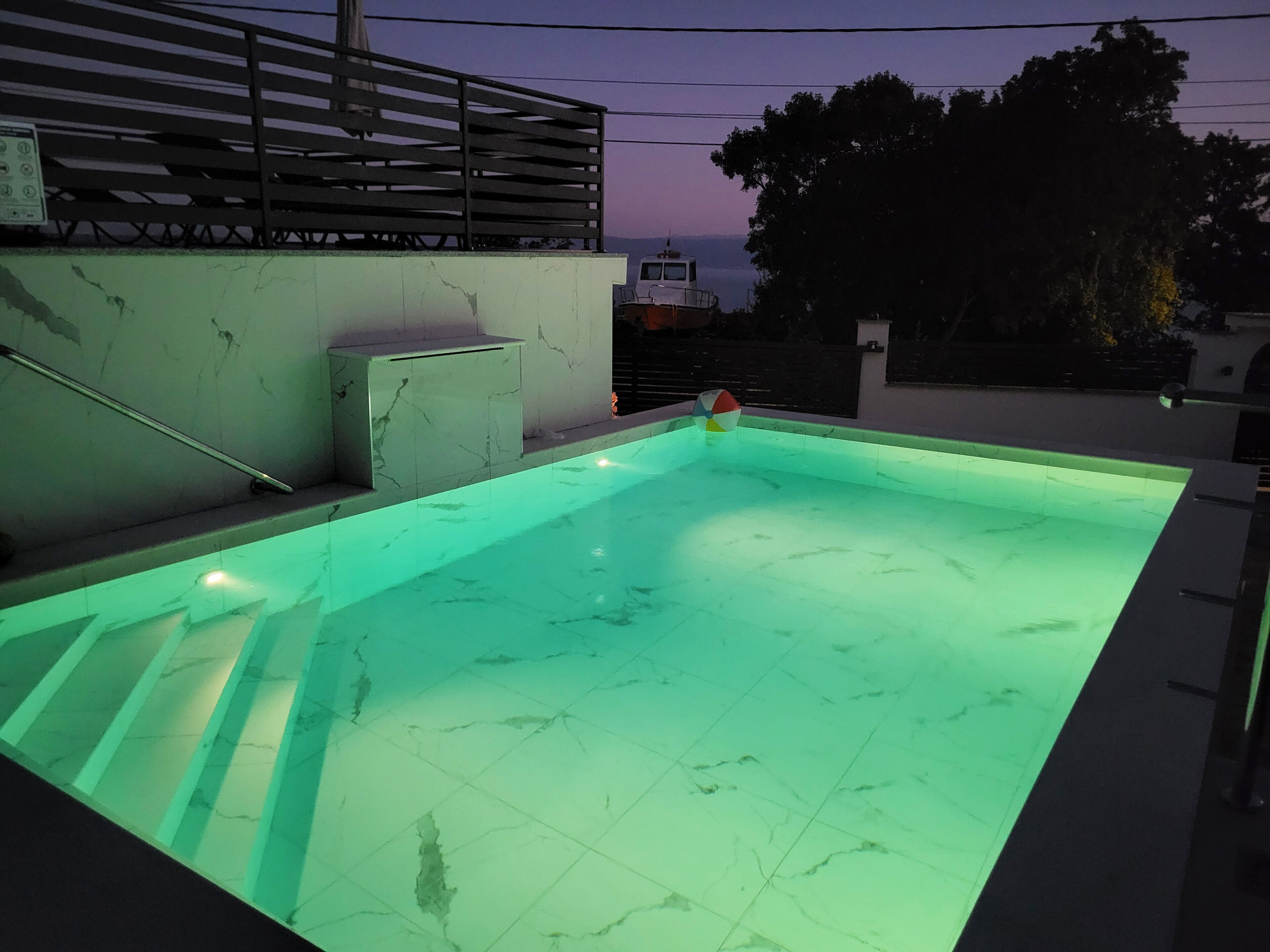 A swimming pool with a green-lit edge, a metal railing, and a bench.