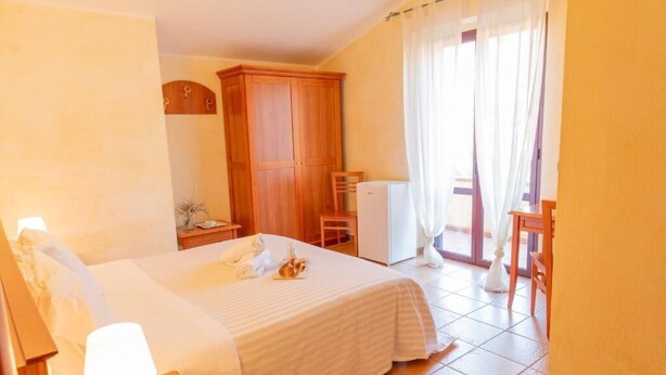 A hotel room with a bed, a desk, a chair, a wardrobe, and a balcony with curtains. - Mediterraneo B&B (Pizzo)