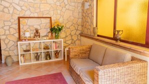 A room with a stone wall, wicker furniture, a white console table with decorative items, and a large window with a golden frame. - Mediterraneo B&B (Pizzo)