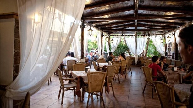 An outdoor restaurant with wicker chairs and tables, covered by a wooden roof and draped with white curtains. - Mediterraneo B&B (Pizzo)