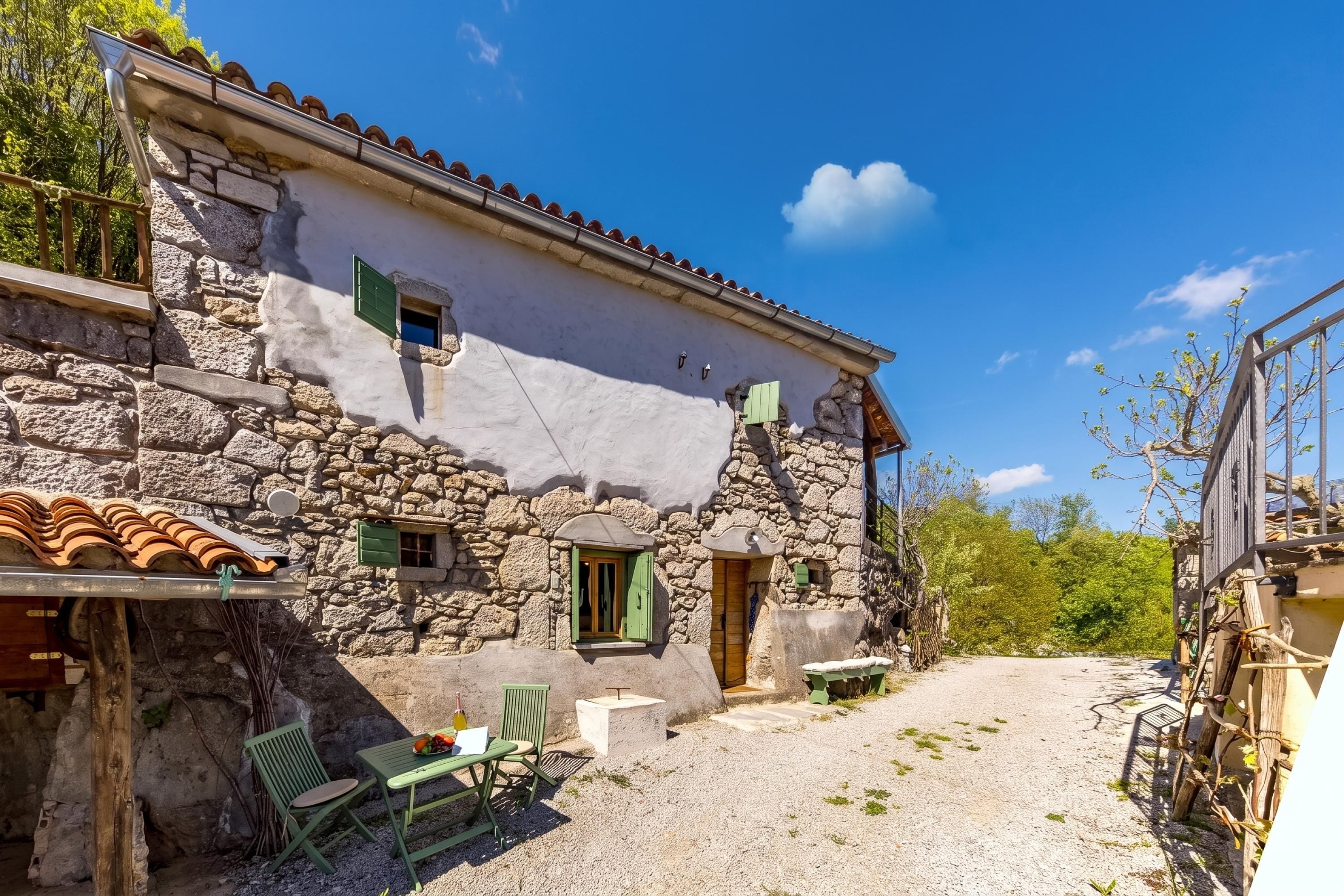 A stone building with a tiled roof, a gravel courtyard, and a small table with chairs.