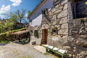 A stone building with a rustic exterior, a wooden door, and a small outdoor seating area with a table and chairs. - Lovrinovi Retreat - Apartment 1 (Matulji)