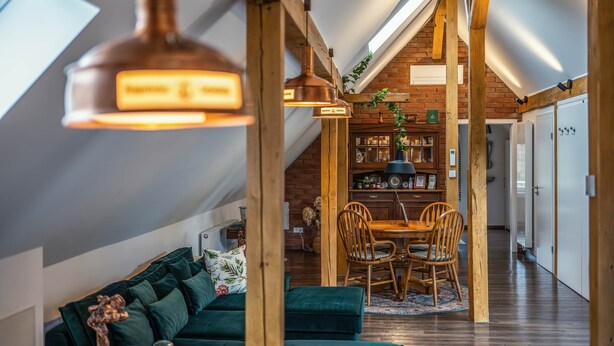Una camera accogliente in stile loft, con divano verde, tavolo da pranzo in legno e illuminazione a sospensione.