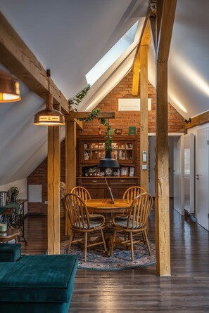 A dining area with a wooden table and chairs, a chandelier, and a brick wall with shelves. - Pine Cone Loft - Peaceful Nature Escape near Baden-Baden (Baden-Baden)