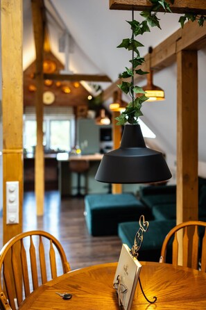 A wooden dining table with chairs, a pendant light with ivy, and a wall-mounted light fixture. - Pine Cone Loft - Peaceful Nature Escape near Baden-Baden (Baden-Baden)