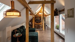 Una stanza in stile loft con travi a vista in legno, una zona pranzo con tavolo e sedie e un angolo relax con divano e poggiapiedi.