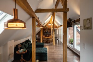 A loft-style room with exposed wooden beams, a dining area with a table and chairs, and a cozy seating area with a sofa and ottoman. - Pine Cone Loft - Peaceful Nature Escape near Baden-Baden (Baden-Baden)