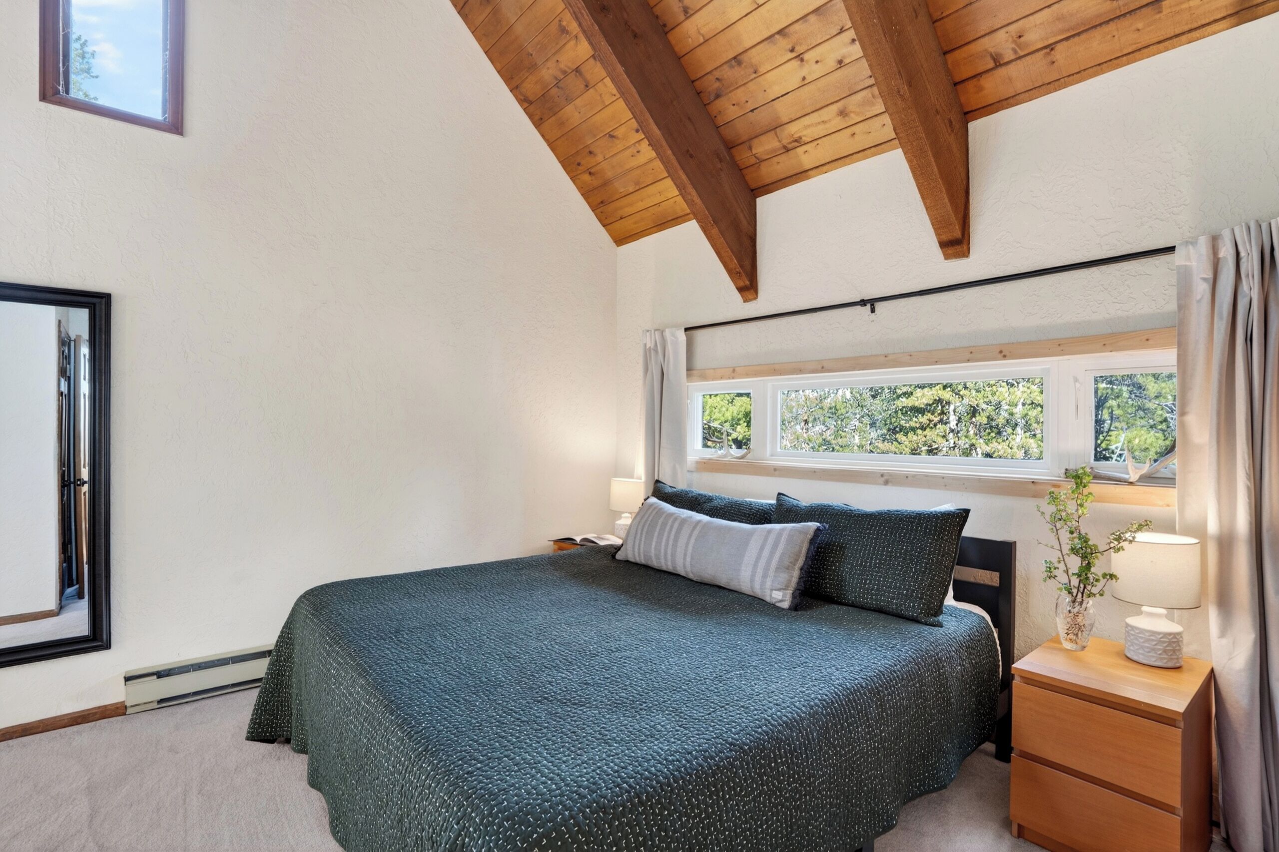 A bedroom with a bed, a nightstand, a window, and a view of greenery outside.