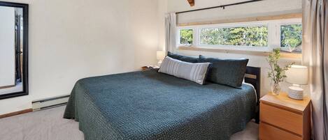 A bedroom with a bed, a nightstand, a window, and a view of greenery outside.