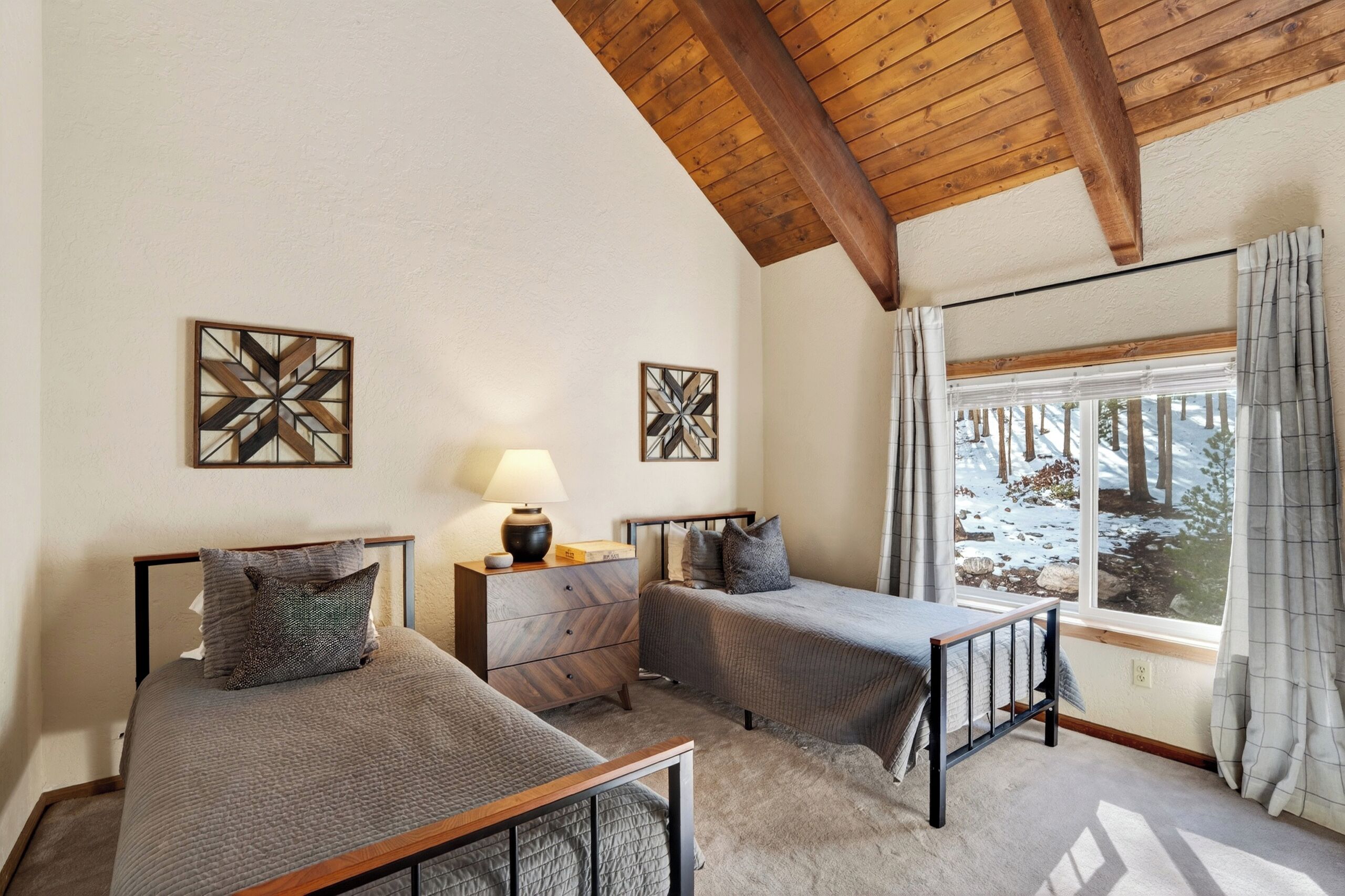Une chambre avec deux lits, une table de chevet, une lampe et une fenêtre avec des rideaux.
