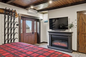 Ein Zimmer mit Kamin, einem darüber angebrachten Fernseher, einer Holztür und einer roten karierten Tagesdecke.