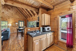 Ein Holzblockhaus-Innenraum mit Küche, Essbereich und einem Fenster mit Vorhängen.