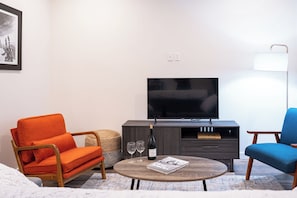 Ein modernes Wohnzimmer mit einer Couch, einem Sessel, einem Couchtisch, einem Fernseher und Weingläsern.