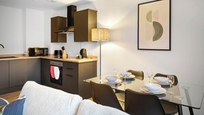 A modern kitchen with a microwave, toaster, and kettle, a dining table set with plates and glasses, and a framed abstract artwork on the wall. - City Point Aberdeeen by Guestz (Aberdeen)