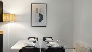 A dining area with a glass table, black chairs, white plates, and a framed abstract artwork on the wall. - City Point Aberdeeen by Guestz (Aberdeen)