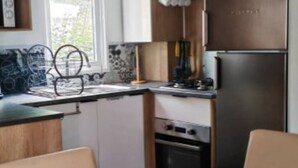 Kompakti keittiö, jossa on modernit kodinkoneet, ruokailutila puupöydällä ja -tuoleilla sekä ikkuna, josta tulee luonnonvaloa.