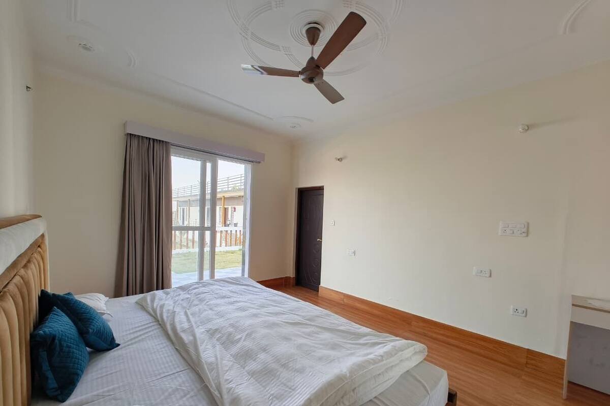 Un dormitorio con cama, ventilador de techo, ventana con cortinas y puerta que da a un espacio exterior.