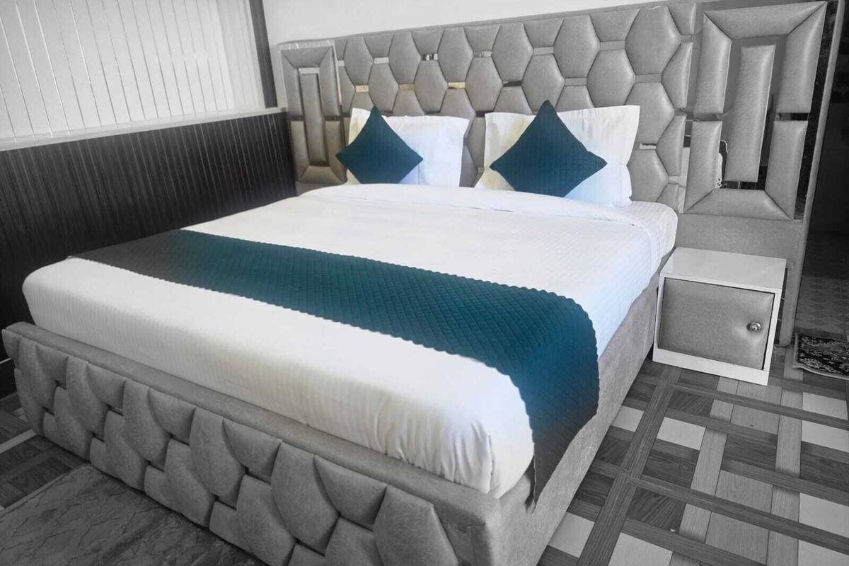 Habitación de hotel con una cama grande, cabecera con diseño geométrico, mesita de noche y piso estampado.