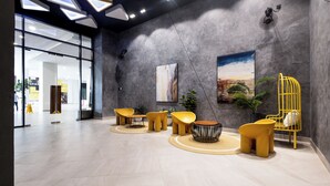 A modern lobby with a large glass entrance, a seating area with yellow chairs, a black and white patterned chair, and a yellow birdcage. - Sunsuria Forum Premier Suites Setia Alam (Shah Alam)