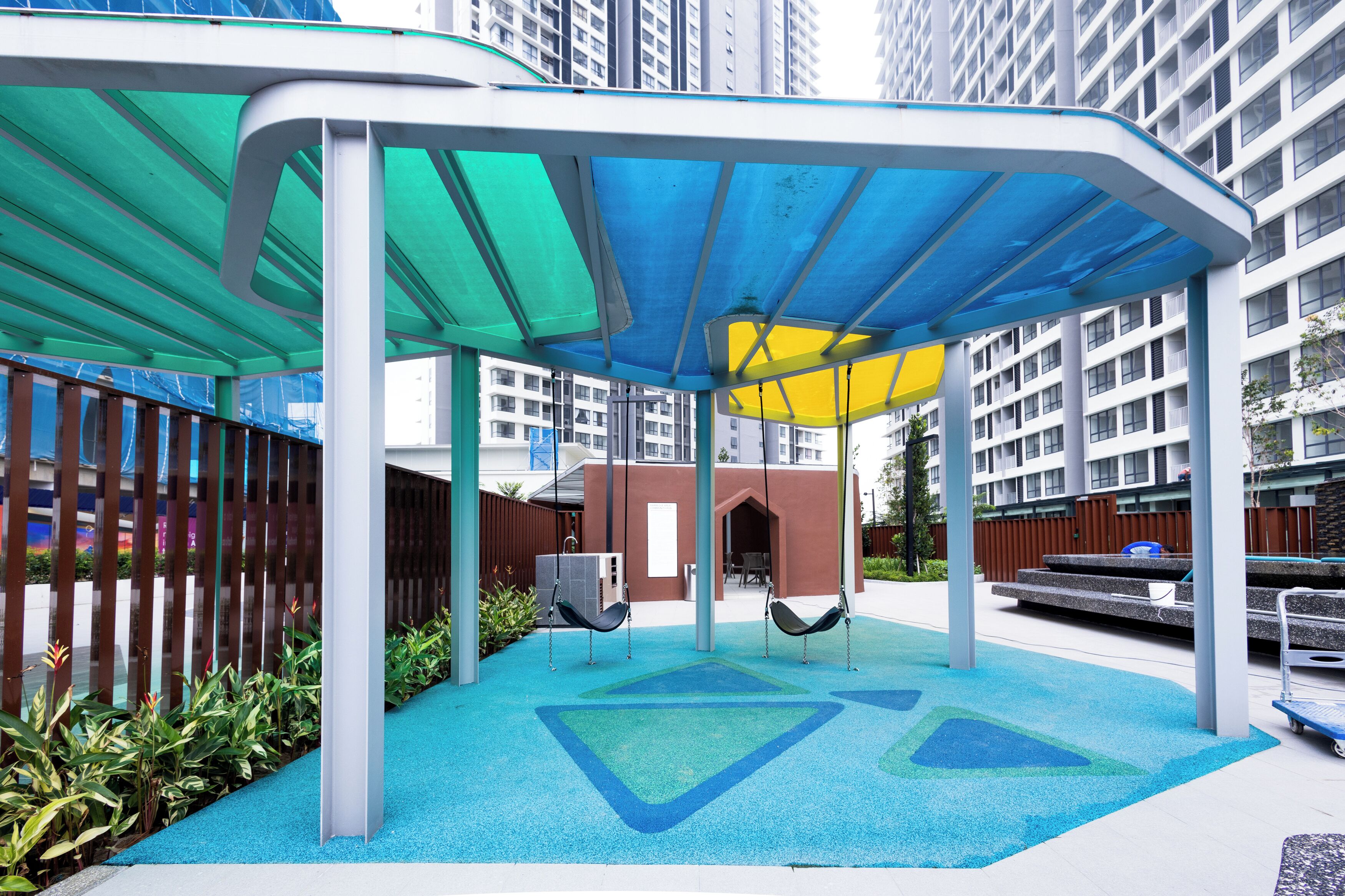 A covered outdoor area with swings, a play area, and a building in the background.