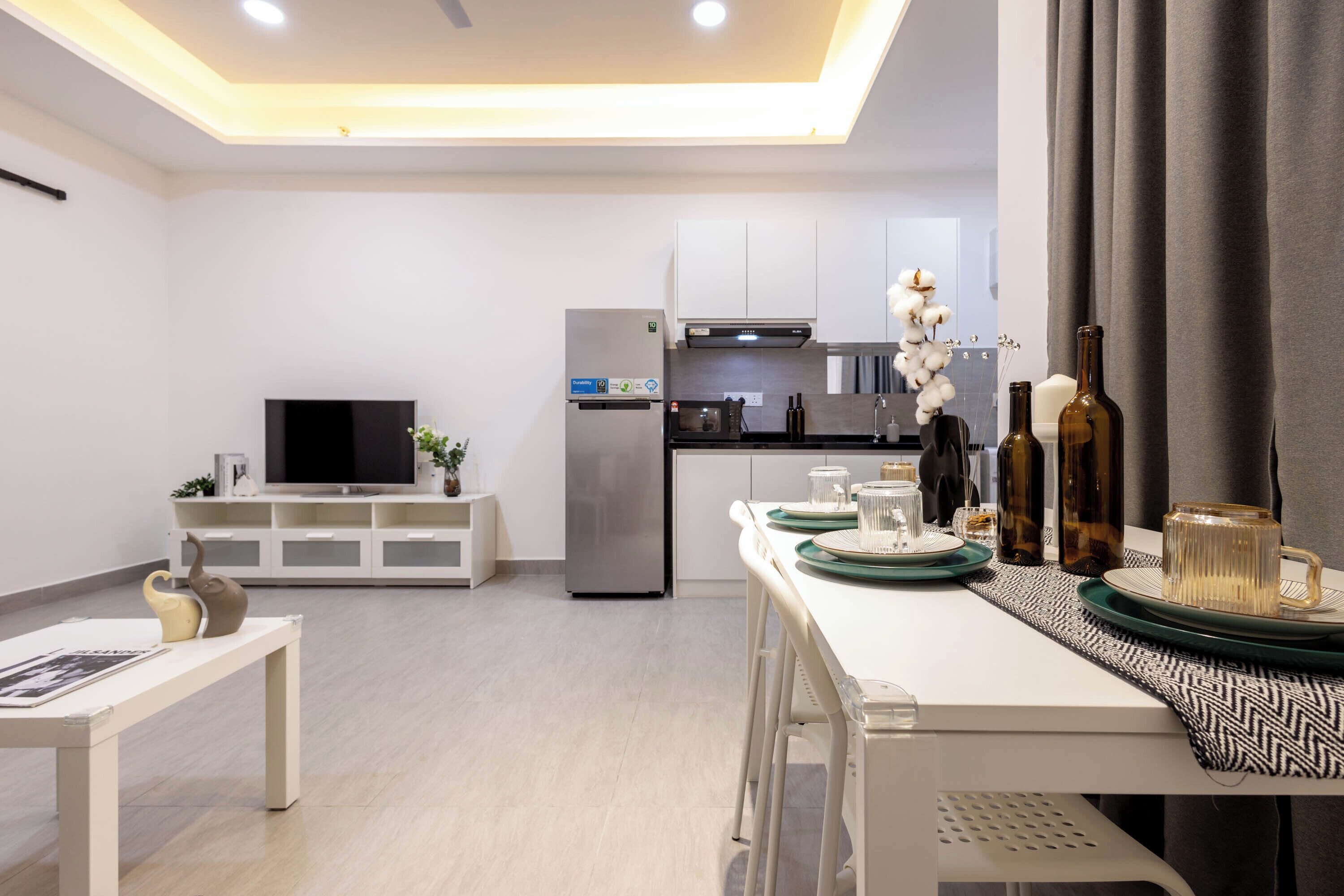 A modern kitchen with a built-in oven, microwave, and refrigerator. There is a dining area with a table set for two, and a television on a stand.