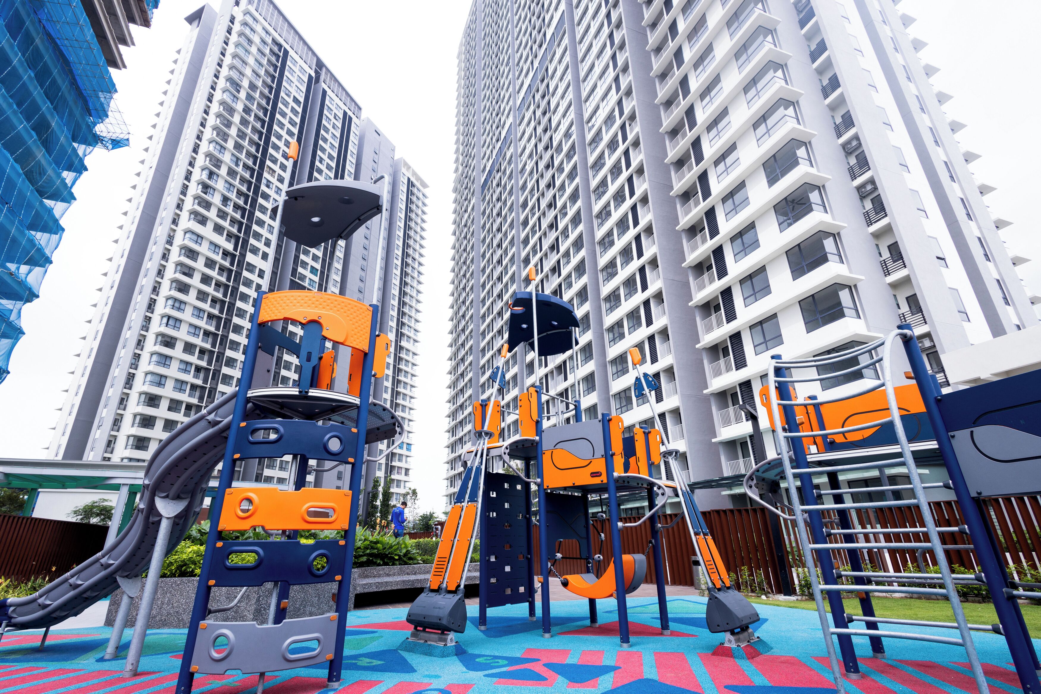 Un parque infantil con estructuras para escalar y toboganes, rodeado de edificios residenciales altos.