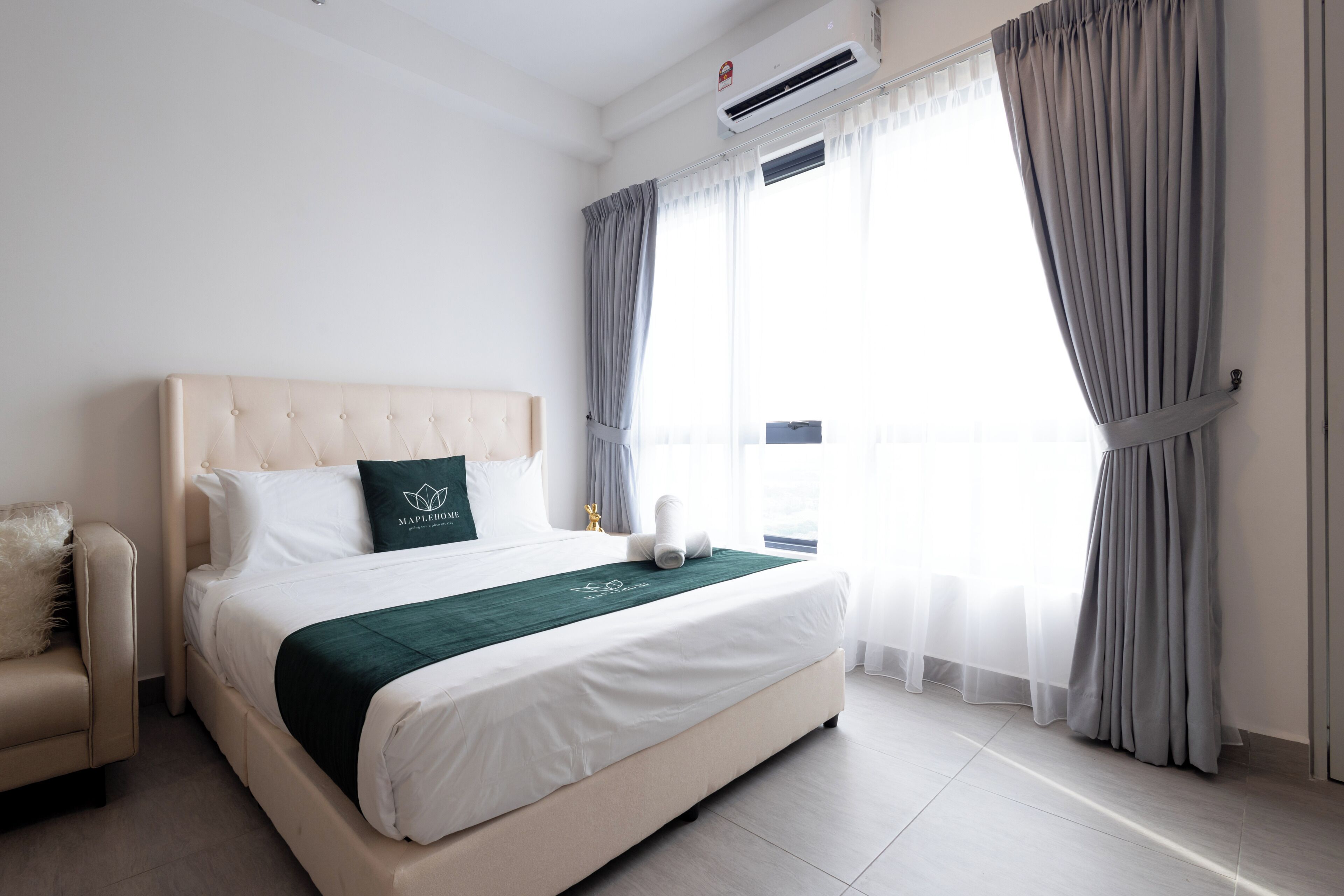 A hotel room with a bed, a chair, a window with curtains, and an air conditioning unit.