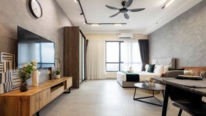 A modern living room with a sofa, TV, ceiling fan, and a large window. - Sunsuria Forum Premier Suites Setia Alam (Shah Alam)