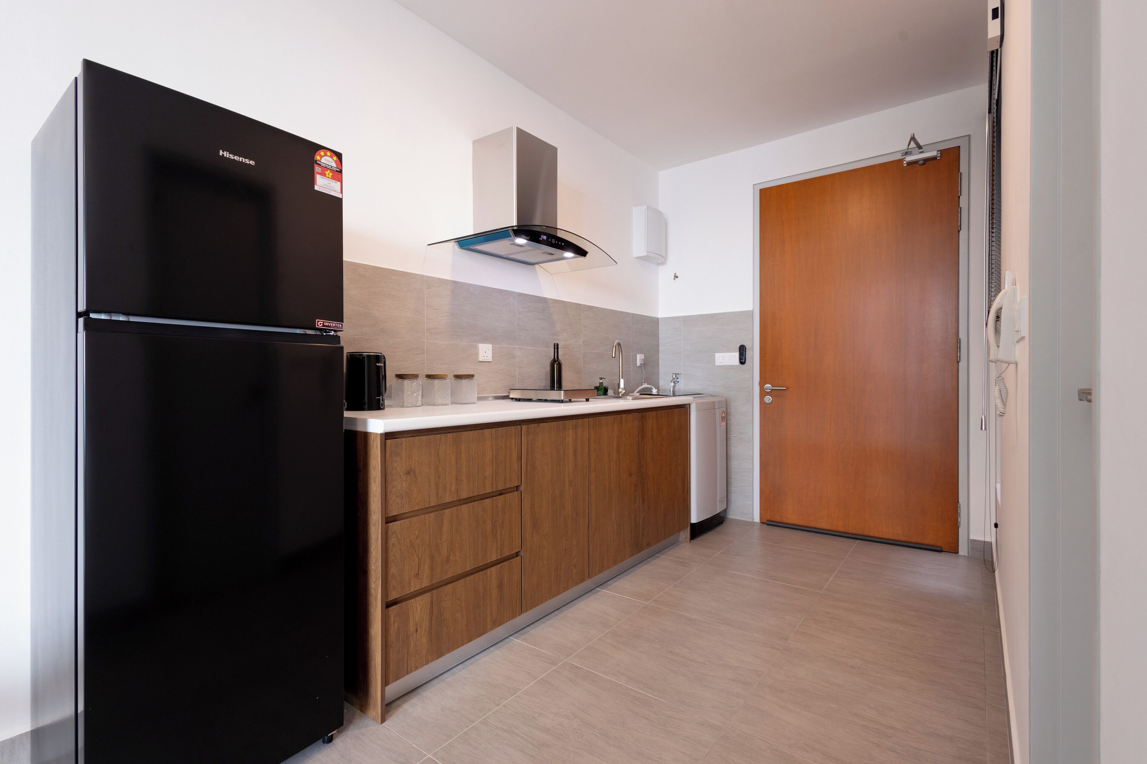 Una cocina moderna con un refrigerador negro, armarios de madera, una campana extractora de acero inoxidable y una puerta de madera.