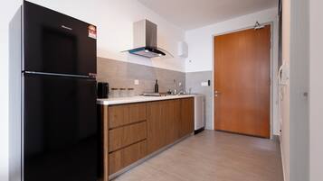 Una cocina moderna con un refrigerador negro, armarios de madera, una campana extractora de acero inoxidable y una puerta de madera.