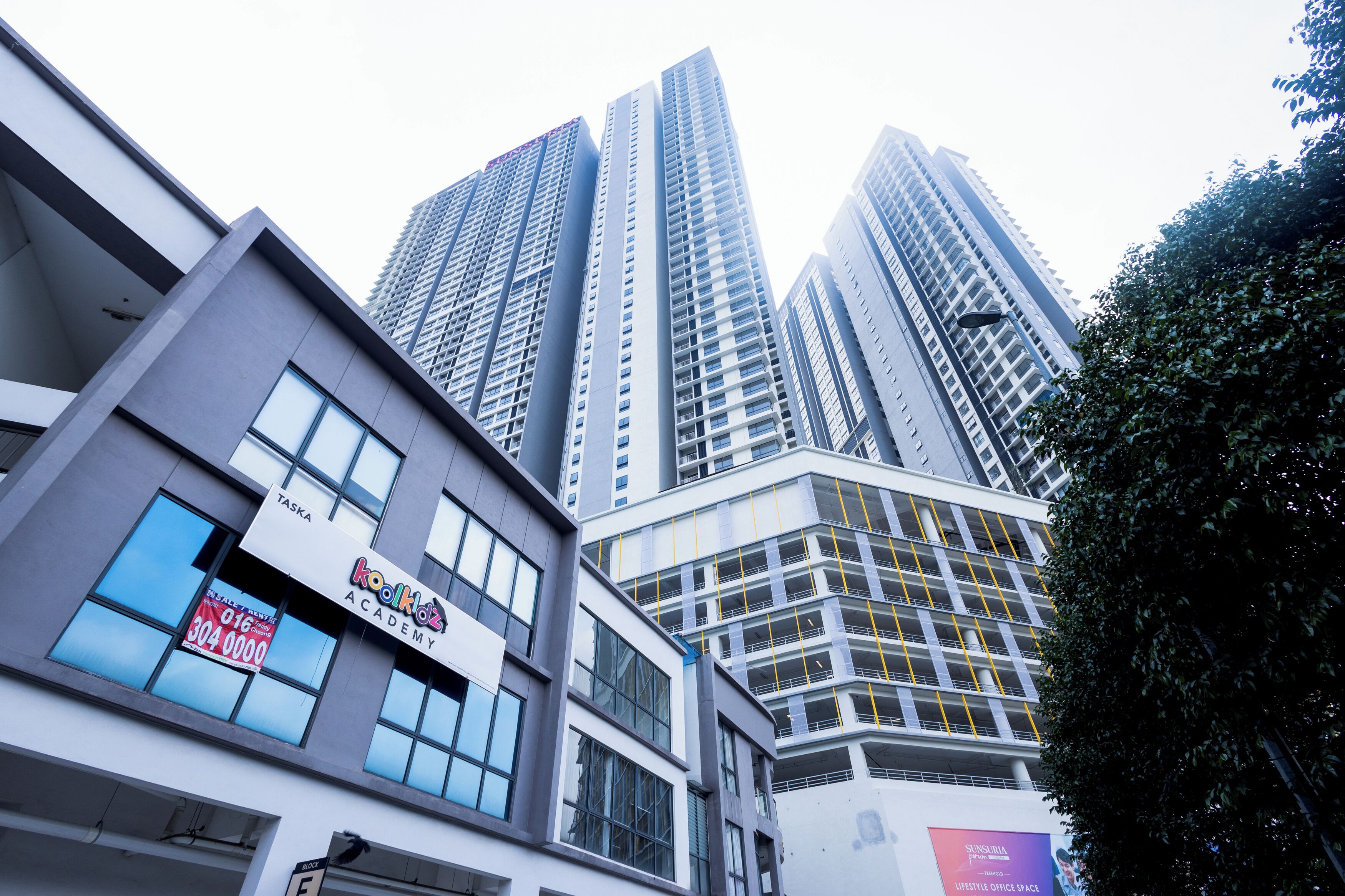 A modern building with a 'Koolhaus Academy' sign, high-rise structures, and a visible 'TASKA' sign.