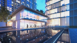 A modern building with a glass facade, outdoor exercise equipment, and a reflective pool.