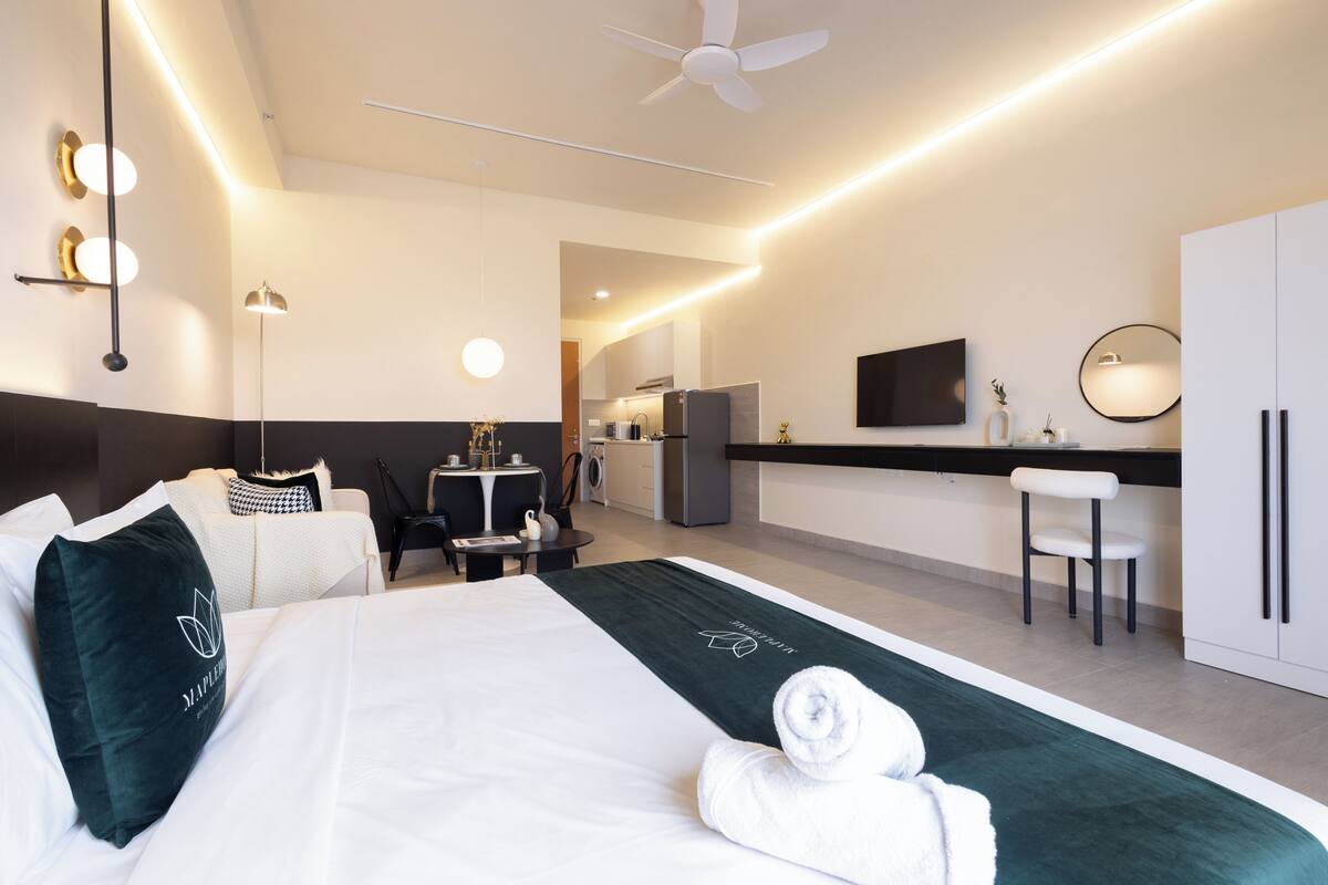 Una habitación de hotel moderna con cama, escritorio, silla, televisor y kitchenette.