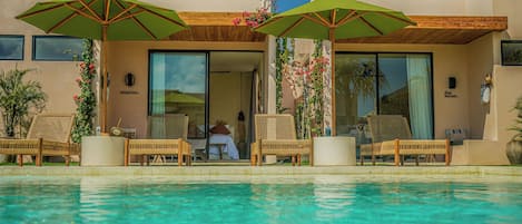 A poolside area with lounge chairs and umbrellas, a clear pool, and a building entrance with glass doors.