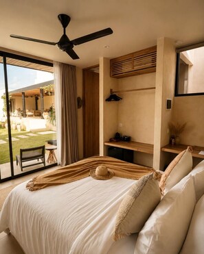 Un dormitorio con cama, ventilador de techo, ventana con cortinas, escritorio con lámpara y vista al exterior.