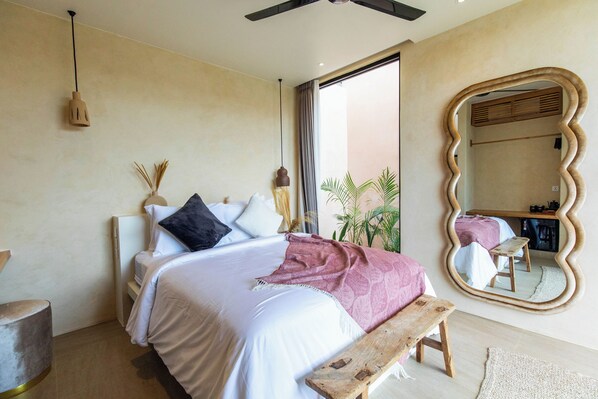 A bedroom with a bed, bedside table, bench, mirror, and a view of the outside. - Nema Uluwatu (Pecatu)