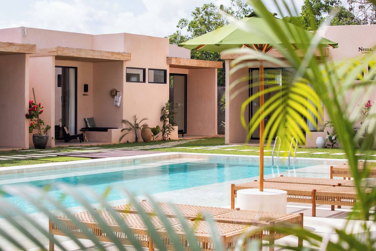 A pool area with lounge chairs, a small patio with a table and chairs, and a building with a door and windows.