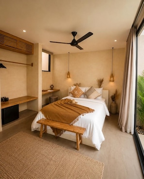 Un dormitorio con cama, mesitas de noche, un banco, ventilador de techo y un ventanal grande.