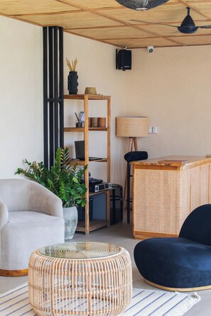 Una sala de estar moderna con un sofá, una mesa de centro de vidrio, una estantería, una lámpara y un sistema de sonido.